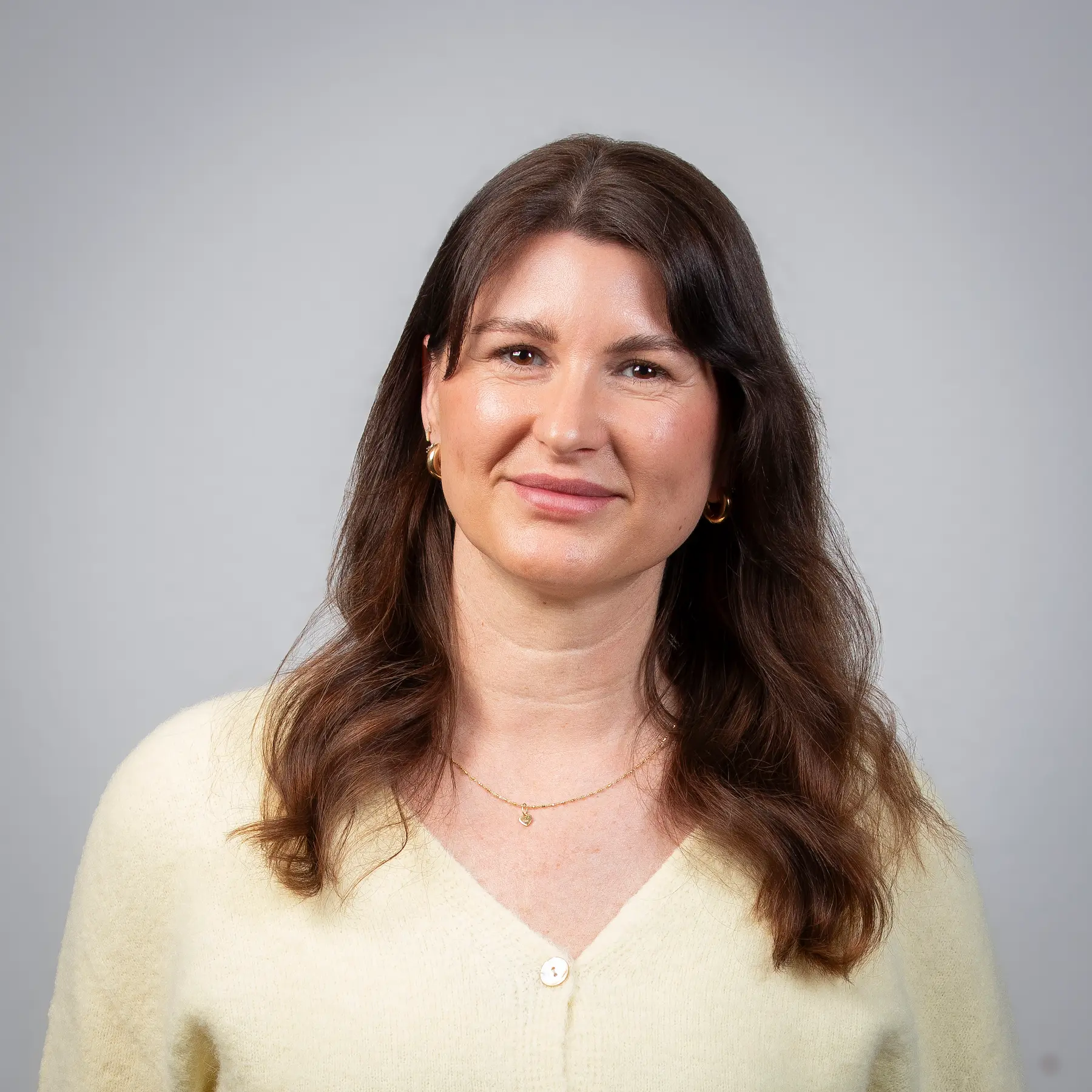 Jannicke Hirsch mit glattem braunem Haar, die einen schwarzen Blazer und ein weißes Hemd mit Kragen trägt, posiert für ein professionelles Portraitfoto vor einem schlichten hellgrauen Hintergrund.