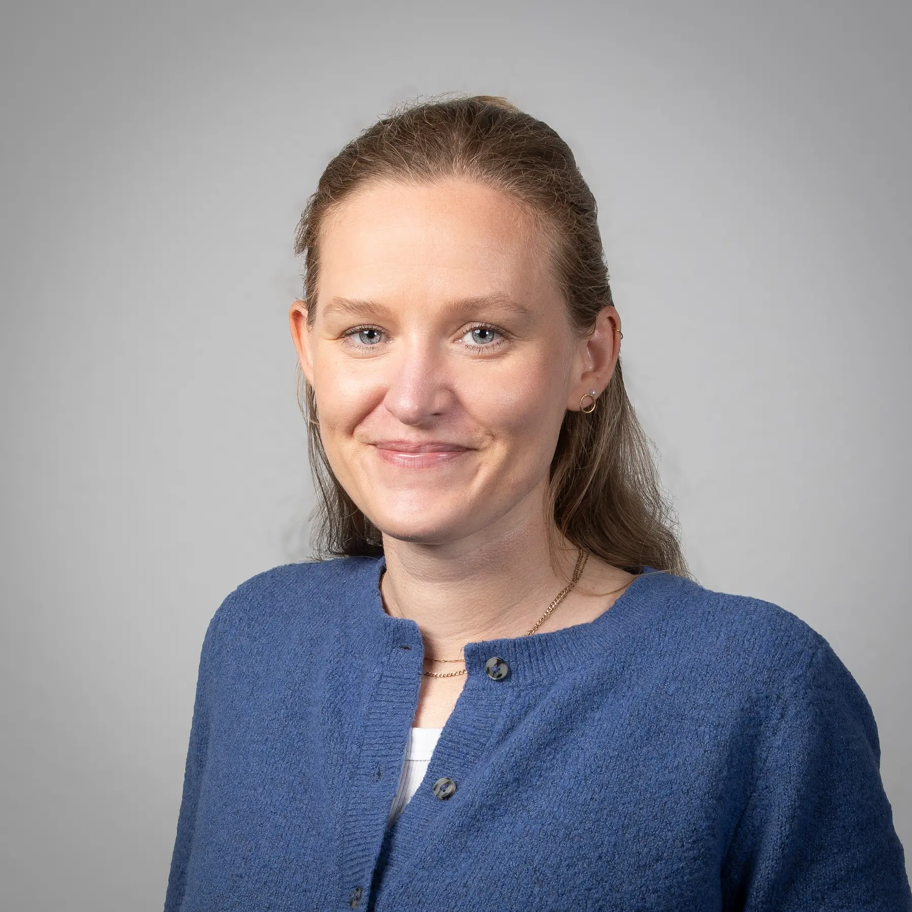 Svenja Held mit blondem Haar und Pony, die einen dunklen Blazer über einem hellen Oberteil trägt, lächelt in die Kamera vor einem schlichten hellen Hintergrund.