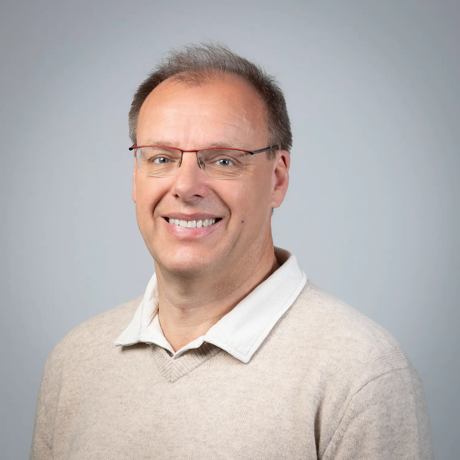 LSB_Mitarbeitende_Thomas_Kaessler Geschäftsführer Thomas Kaessler, der eine Brille und ein weißes Hemd trägt, lächelt in die Kamera vor einem schlichten grauen Hintergrund.