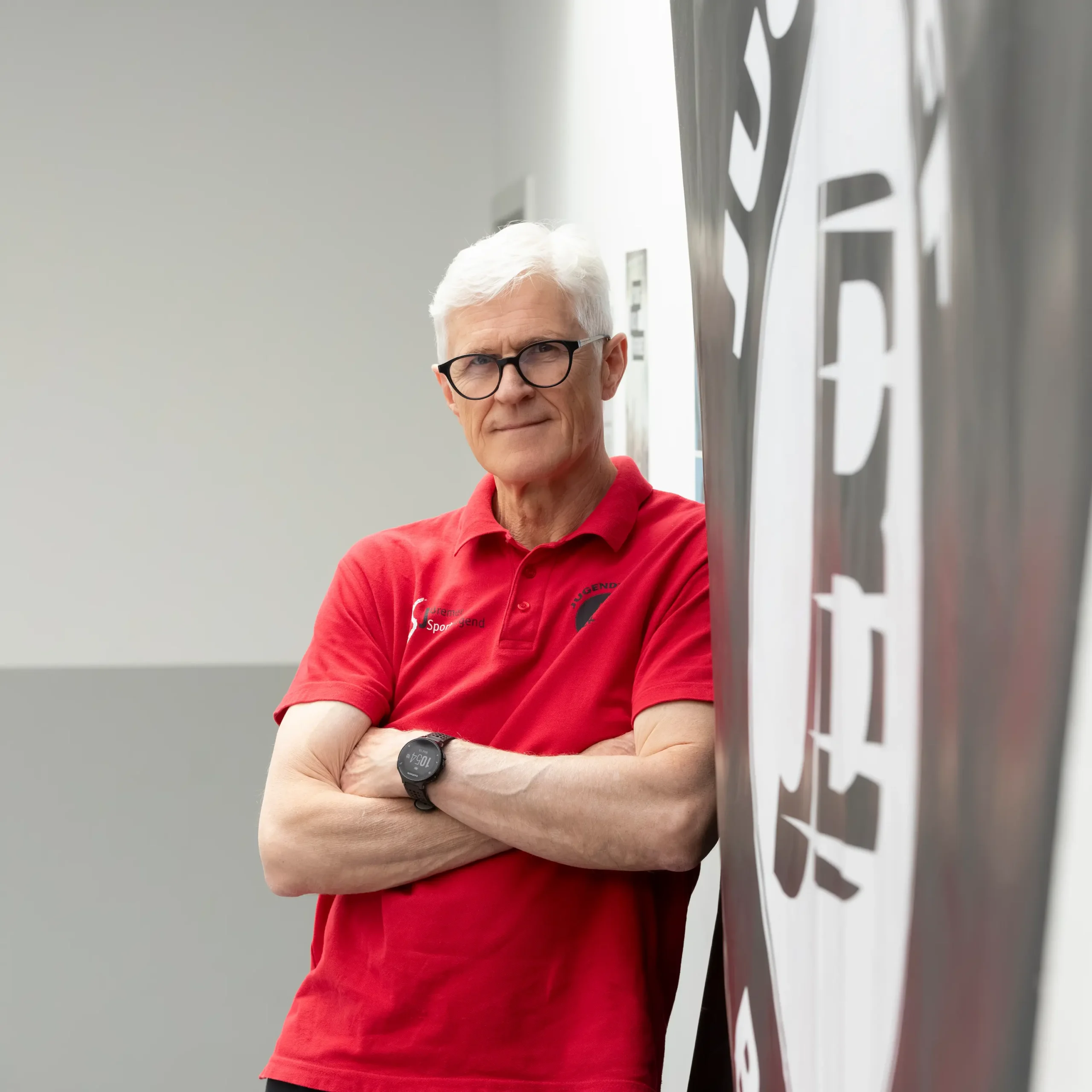 Ein lächelnder Marek Kepinski mit kurzen weißen Haaren, der einen dunklen Blazer und ein weißes Hemd trägt, posiert vor einem schlichten hellen Hintergrund mit dem Logo des Jugendtreffs Blockdiek.