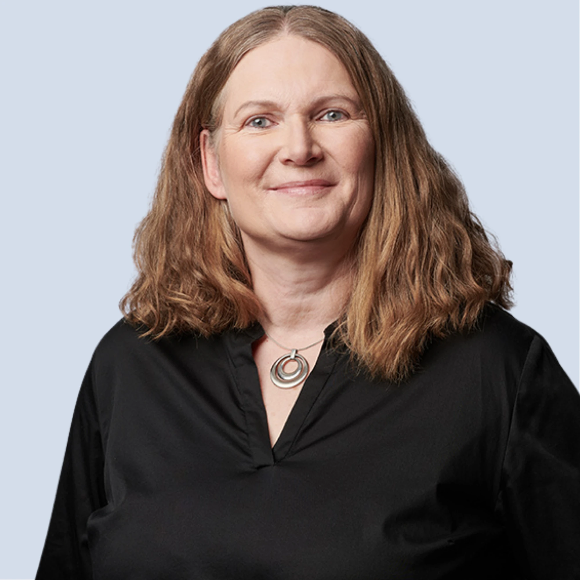 LSB_Hauptausschuss_Heike_Kretschmann Heike Kretschmann lächelt in die Kamera, silberne Kette, Portrait vor einem hellblauen Hintergrund
