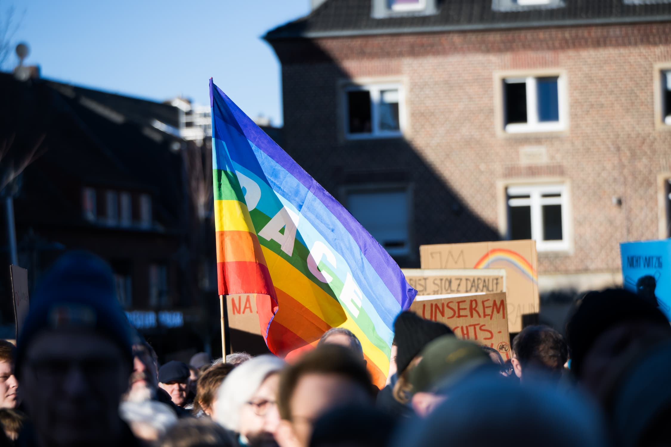 Menschenmenge protestiert auf der Straße, zentral im Foto ist eine Regenbogen-Flagge
